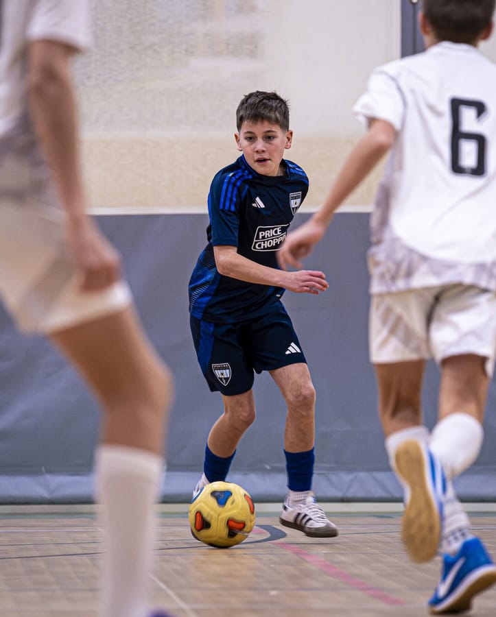 An SBV player in the navy kit dribbling past a player in white